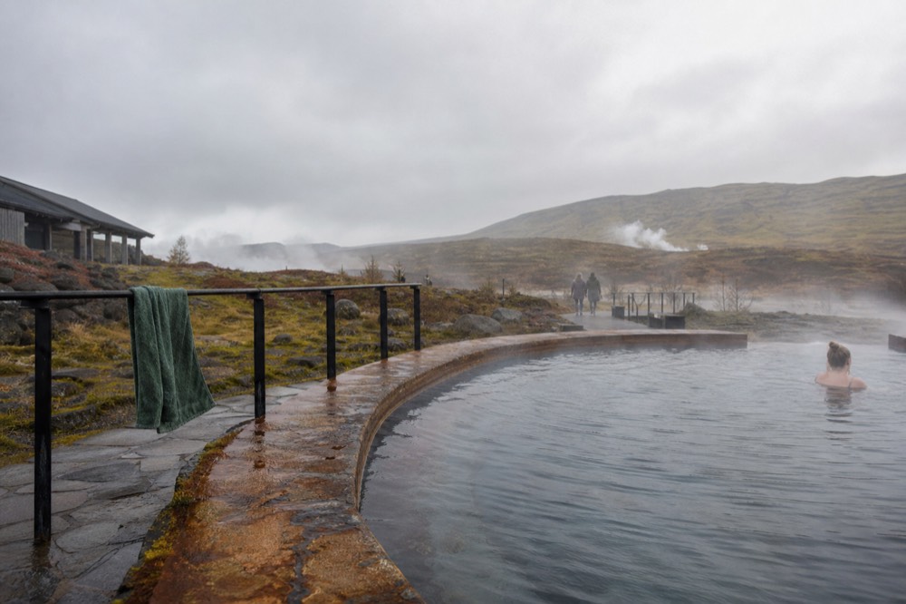 A calm geothermal pool with steam drifting across still water