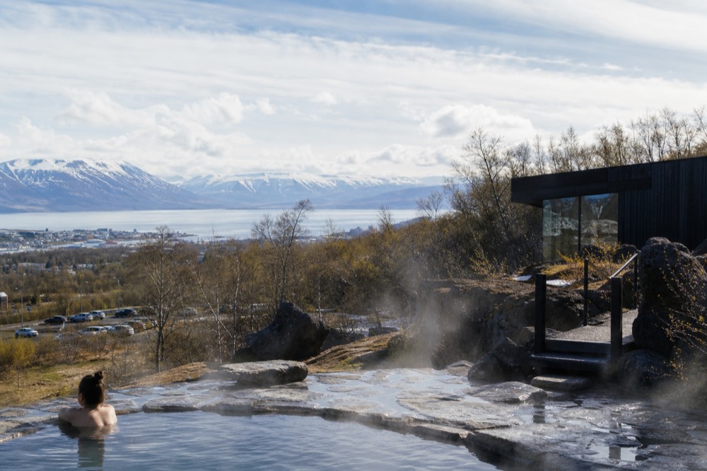 Steaming hot pools built into dark volcanic rock beside a lake