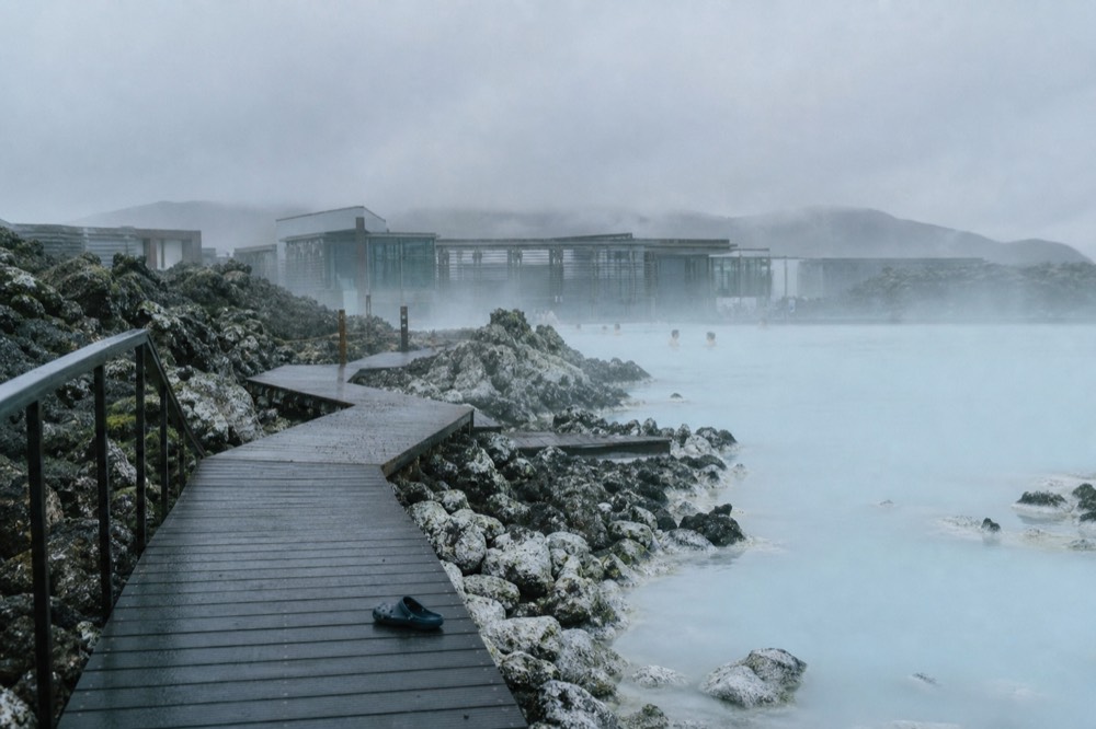 A wooden walkway leading to a steaming geothermal pool in a lava field
