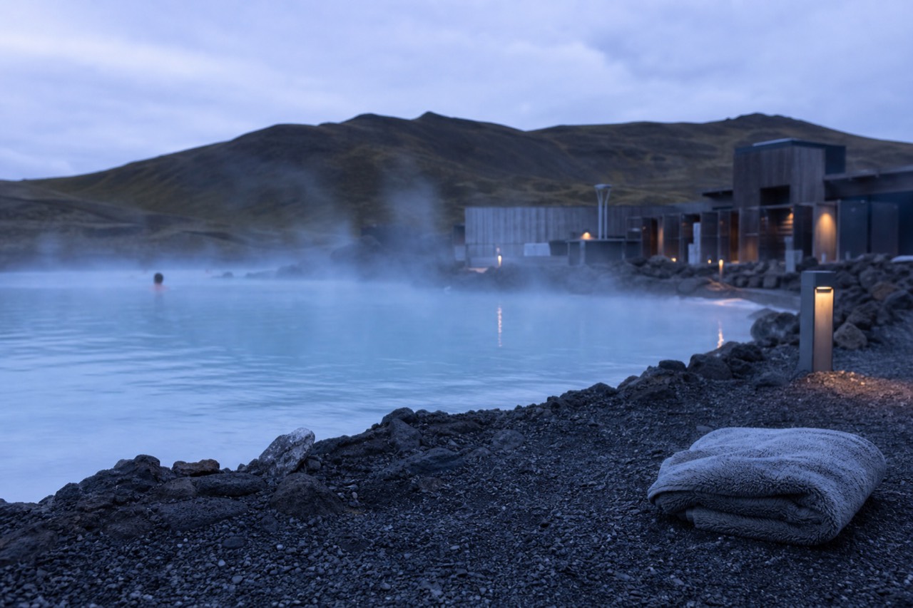 Steam rising from a geothermal lagoon at dusk with dark hills behind it