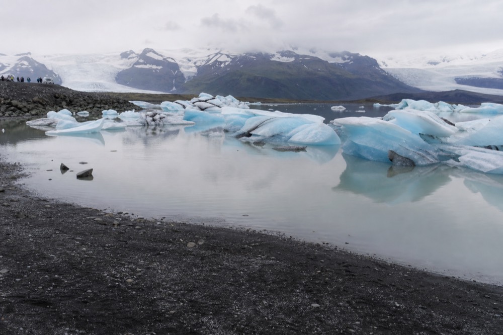 Large blue and white icebergs drifting on still grey water with black sand shore