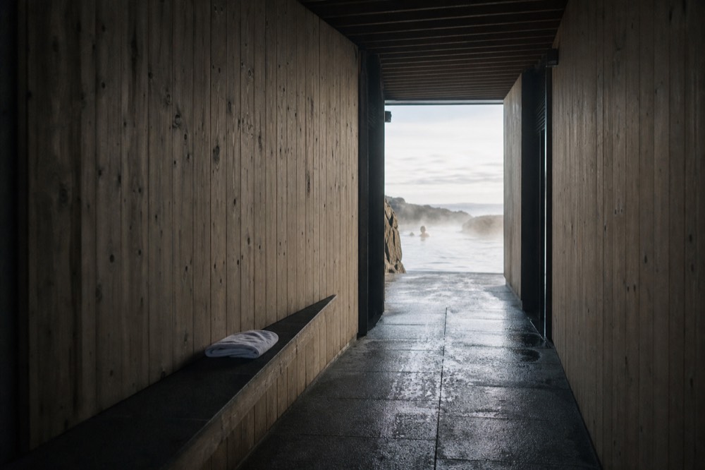 A covered walkway leading from changing rooms toward a steaming oceanfront lagoon