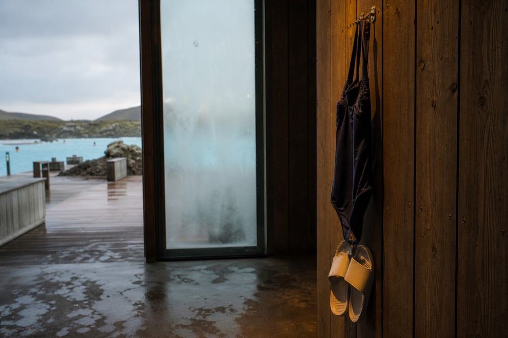 A swimsuit and sandals hanging to dry on a hook beside a warm pool