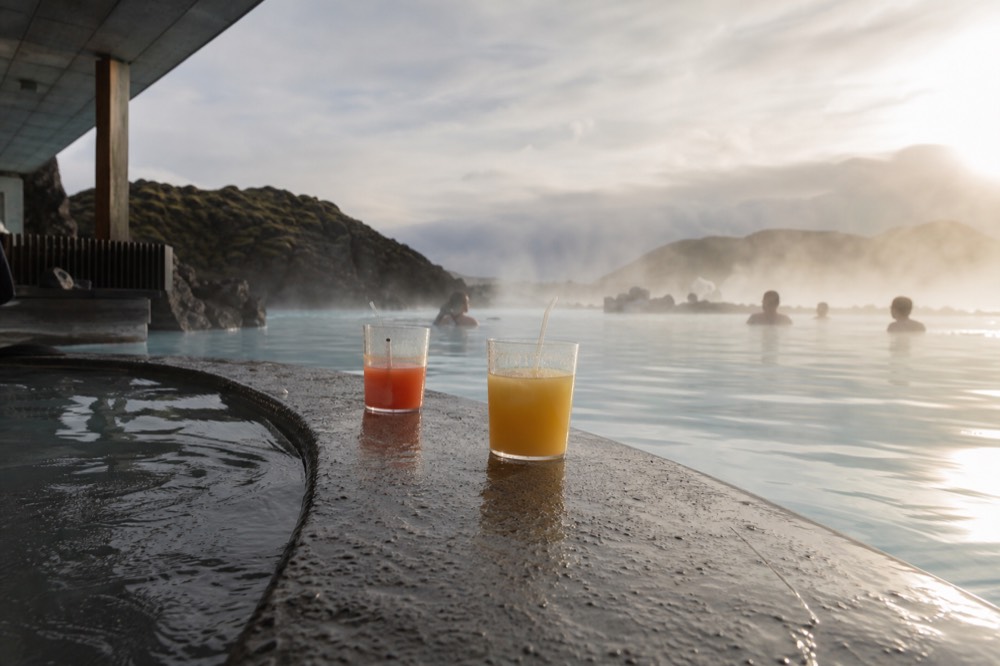 In-water bar counter with drinks beside a steaming lagoon edge