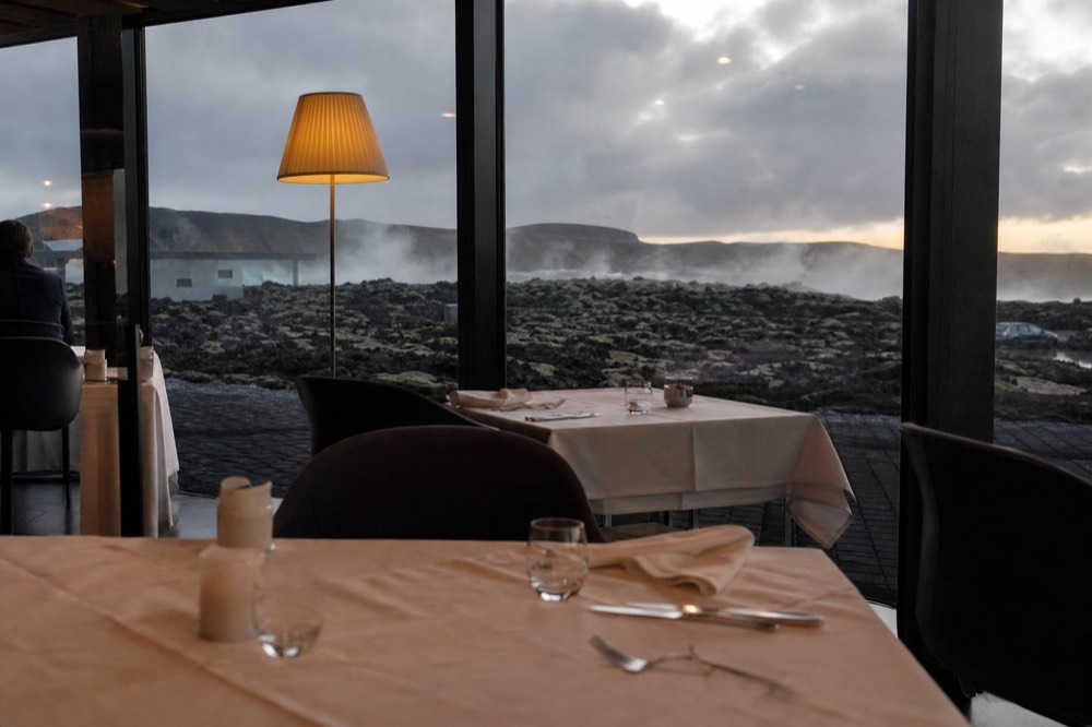 Restaurant dining room with floor-to-ceiling windows facing a dark lava field