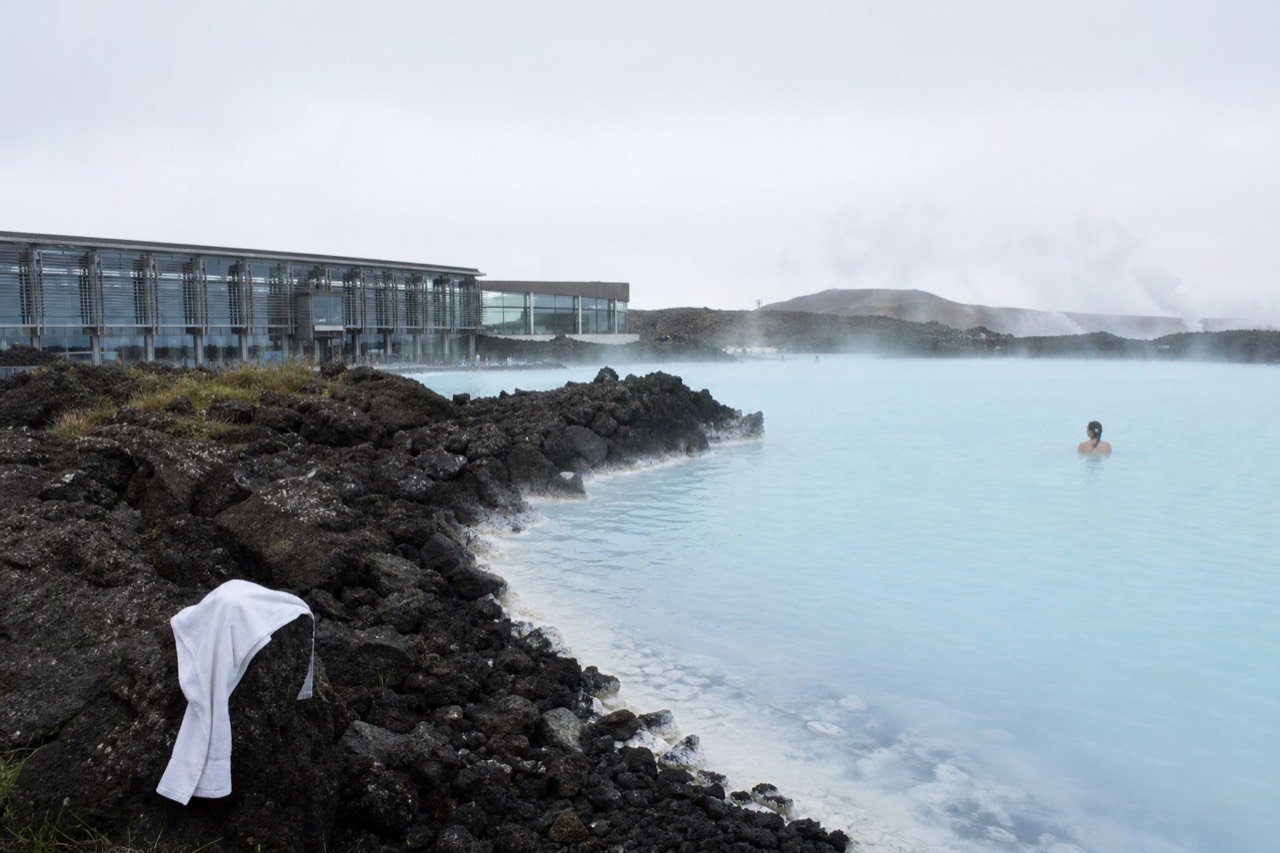 Steaming blue geothermal lagoon beside a modern restaurant building on a lava field