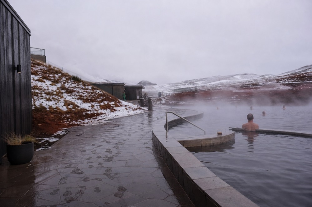 Steam drifting across a geothermal pool surrounded by snow-flecked ground