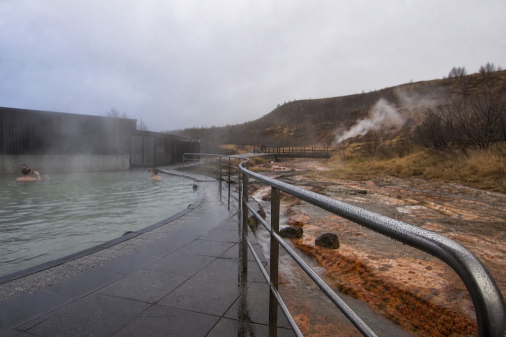 A geothermal pool beside a fjord with still water and low hills in the distance