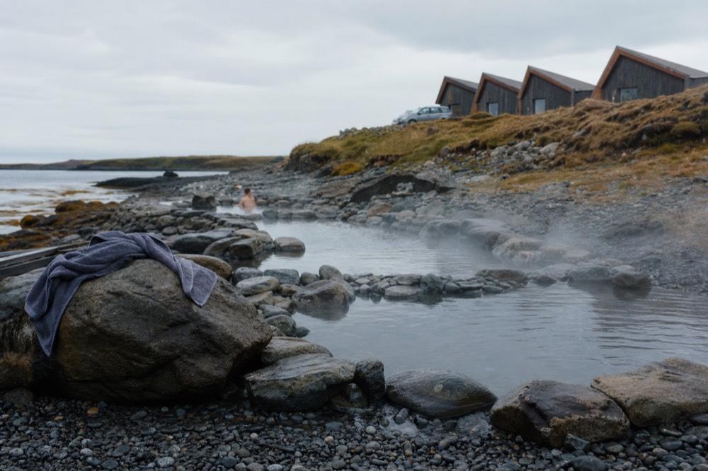 Rock pools of steamy geothermal water built into a dark stony shoreline