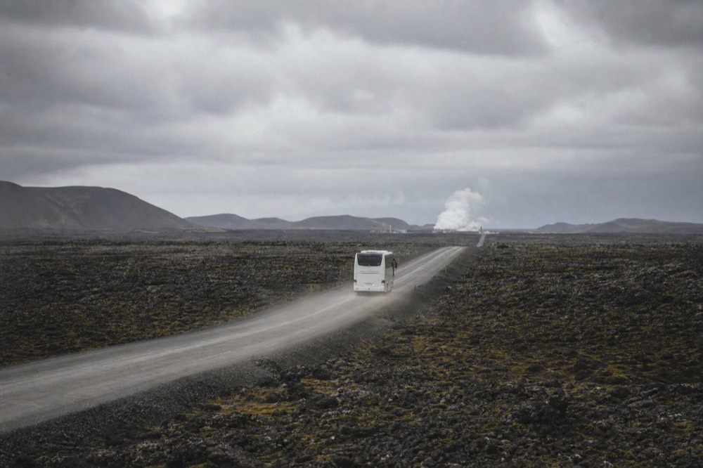 A coach travelling a straight road across a wide plain of dark lava rock