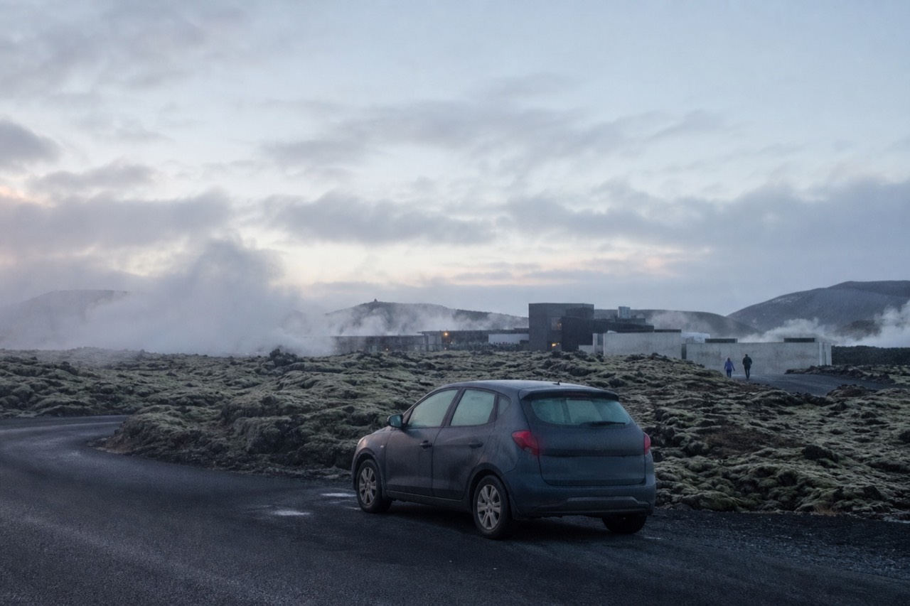Geothermal steam rising over a dark lava field beside a quiet coastal road in southwest Iceland