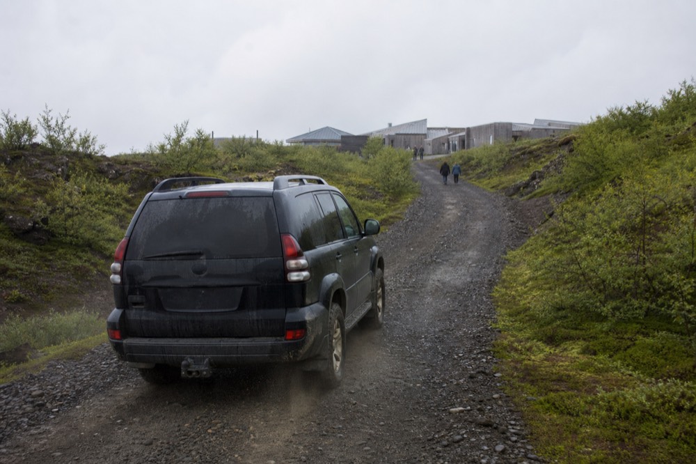 A rugged four-wheel-drive vehicle on a narrow gravel track between mossy hills