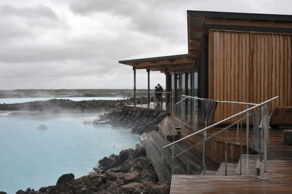 A modern timber spa building above a steaming geothermal lagoon in North Iceland