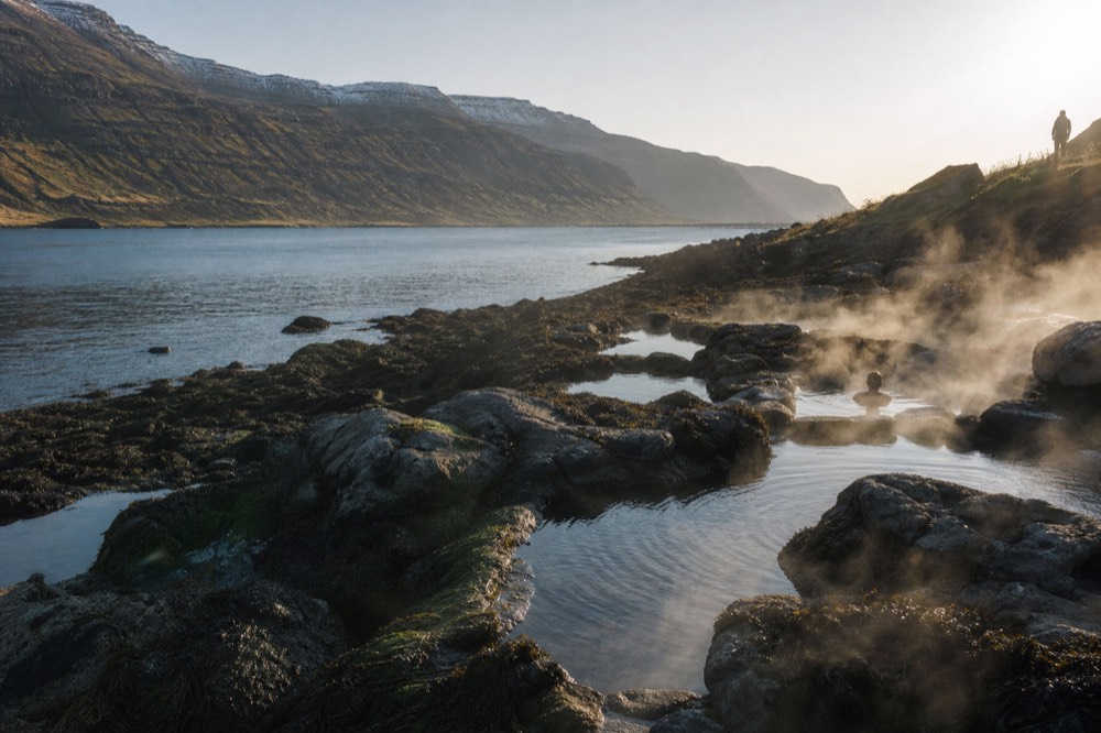Natural stone pools of varying sizes on a fjord shoreline with steam rising