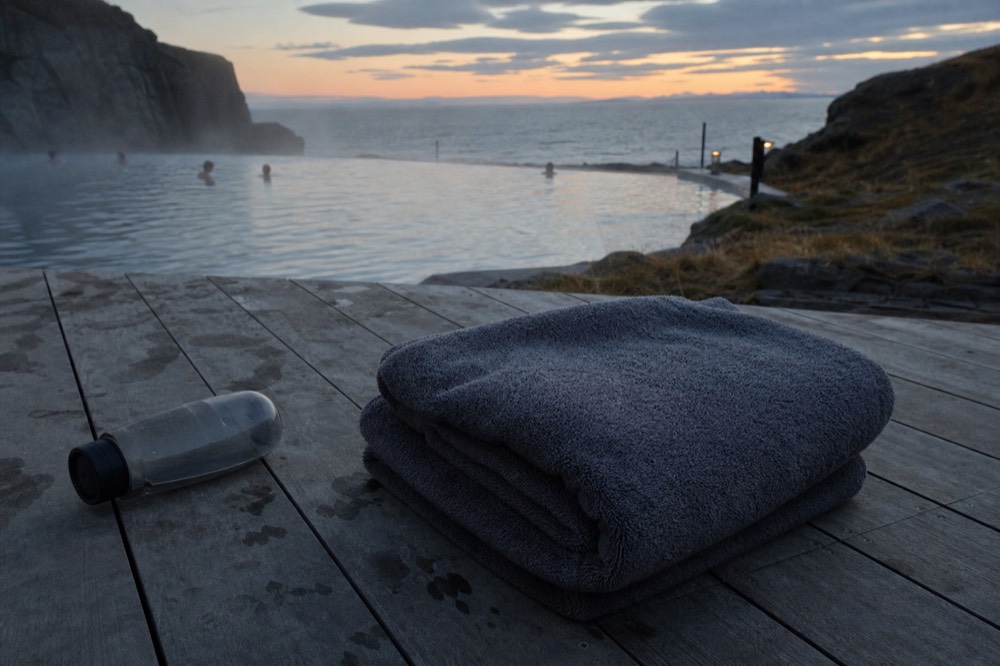 Towel folded on a wooden bench beside a steaming outdoor pool at dusk