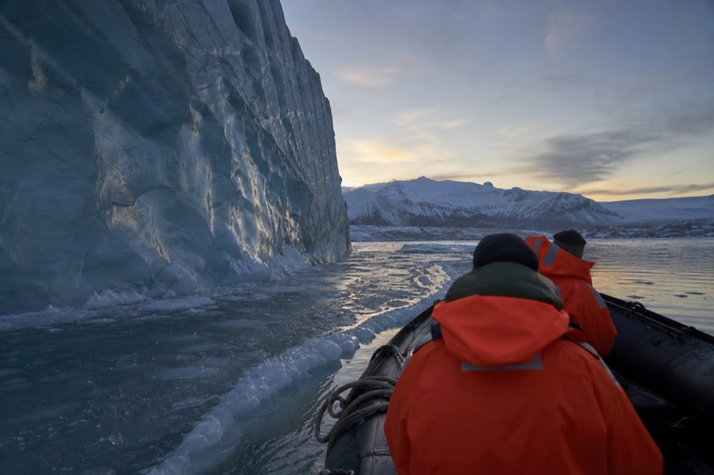 A Zodiac boat holding passengers in orange flotation suits gliding past tall icebergs