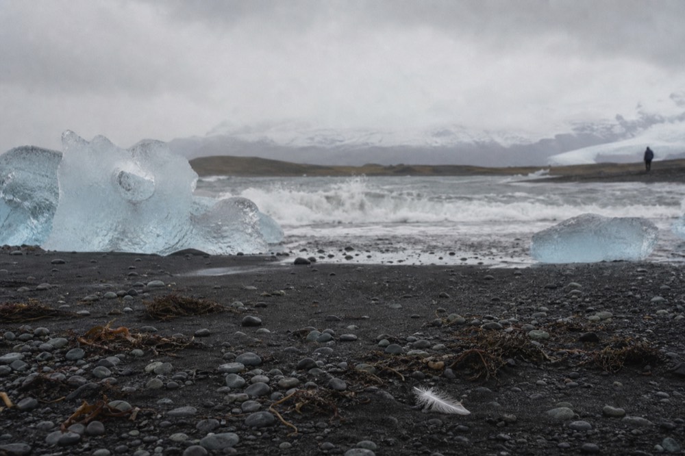 Icebergs grounded on black sand beside grey Atlantic surf at the edge of a glacier lagoon