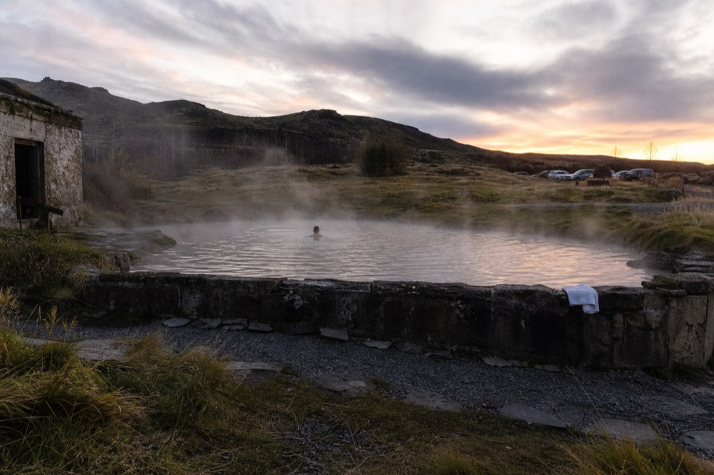 Steam rising from a geothermal pool at dusk with dark hills behind