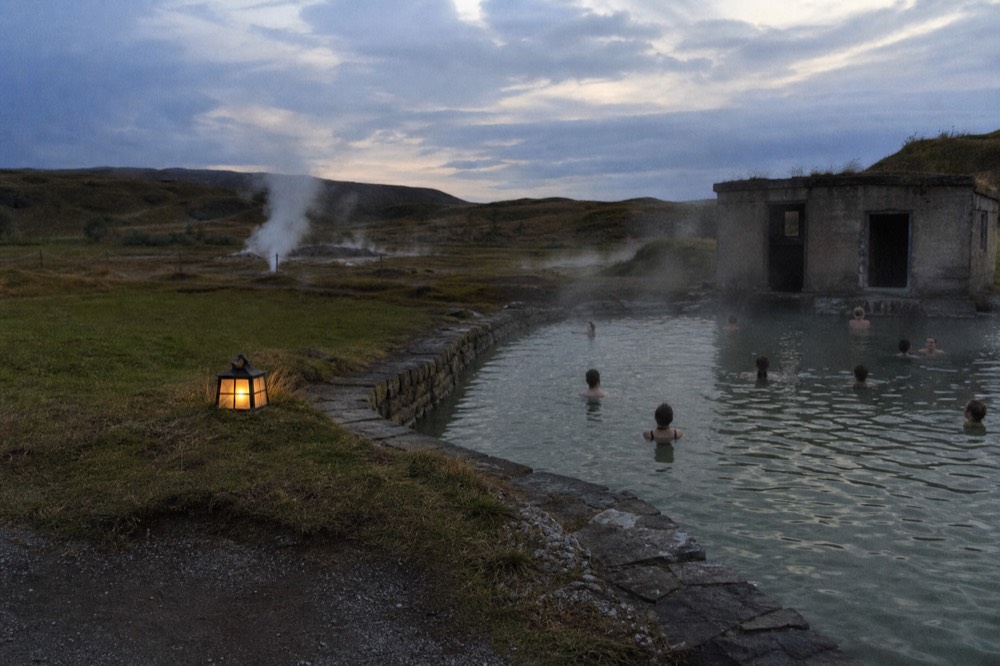 A calm geothermal pool at dusk with steam lifting from the surface into cool air
