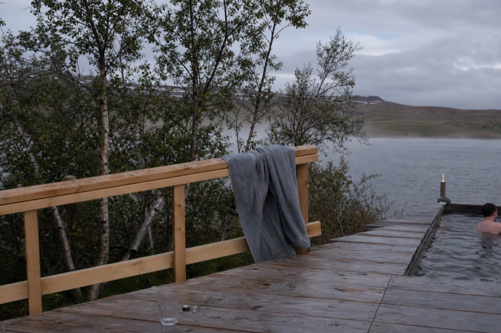 A wooden deck beside steaming geothermal water with a towel draped over a rail