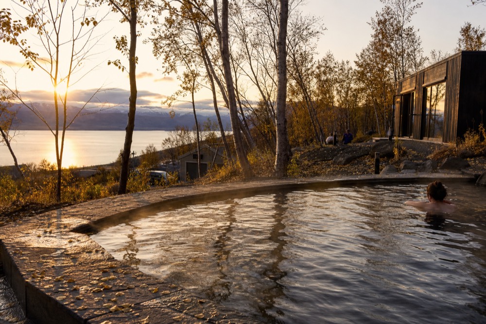 A quiet geothermal pool at the edge of a forested hillside in evening light
