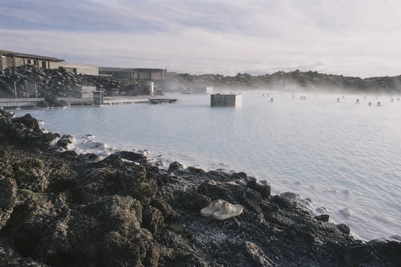 Steam rising from a milky blue geothermal lagoon spread across a dark lava field