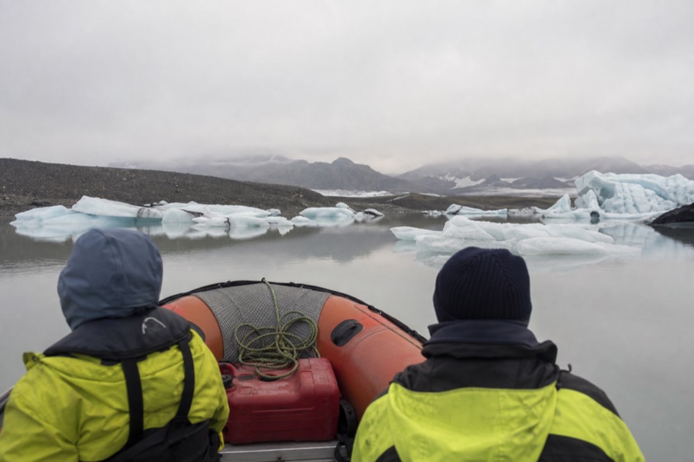 Small orange Zodiac boat moving between flat icebergs on a still glacial lagoon