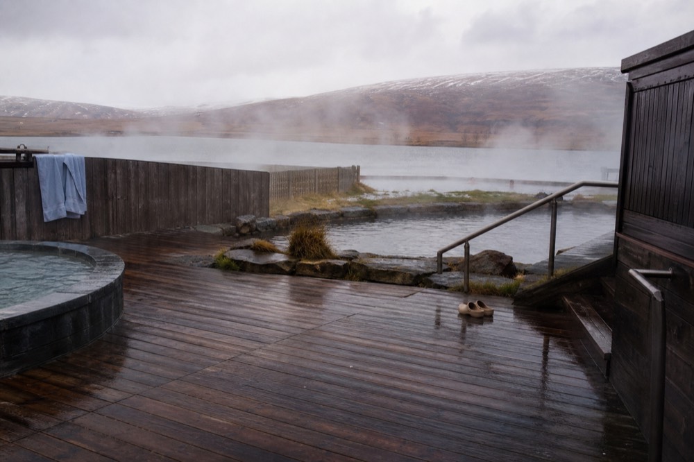 A wooden deck between geothermal pools and a calm lake with steam drifting across the water