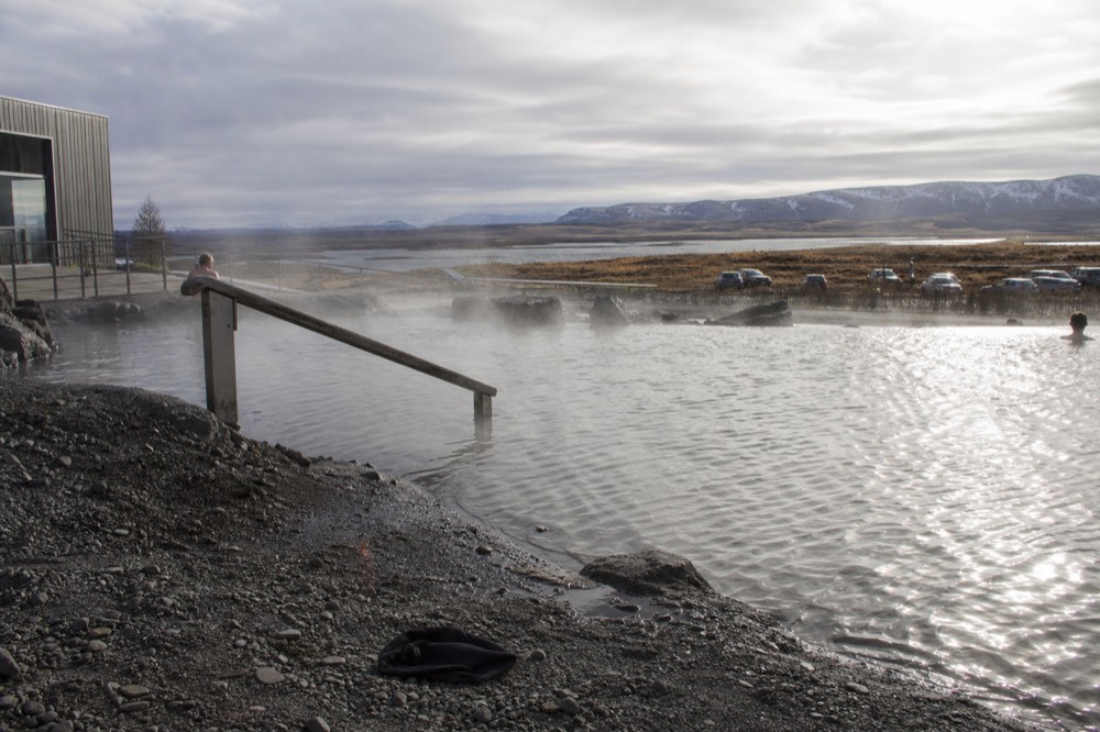 Steam drifting from pools beside a lake with a glacier-fed river plain beyond