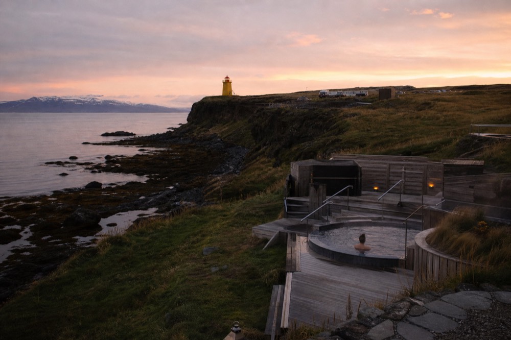 Geothermal pools on a coastline beside a yellow lighthouse under an evening sky