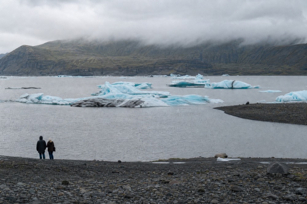 A wide cold lake dotted with white and blue icebergs under an overcast sky