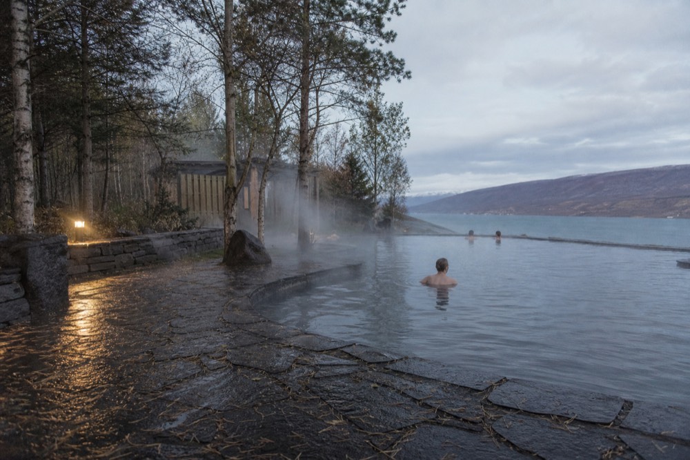 Bathers shoulder-deep in a steaming turquoise pool with a wooden sauna behind