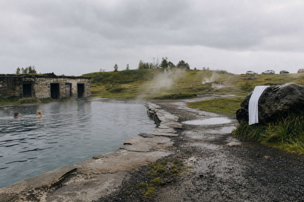 A stone-edged warm pool steaming beside a grassy geothermal field