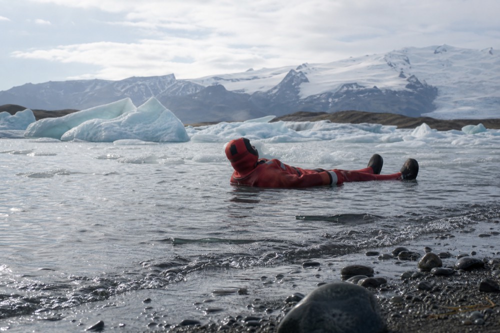 A person in a red immersion suit floating among small icebergs