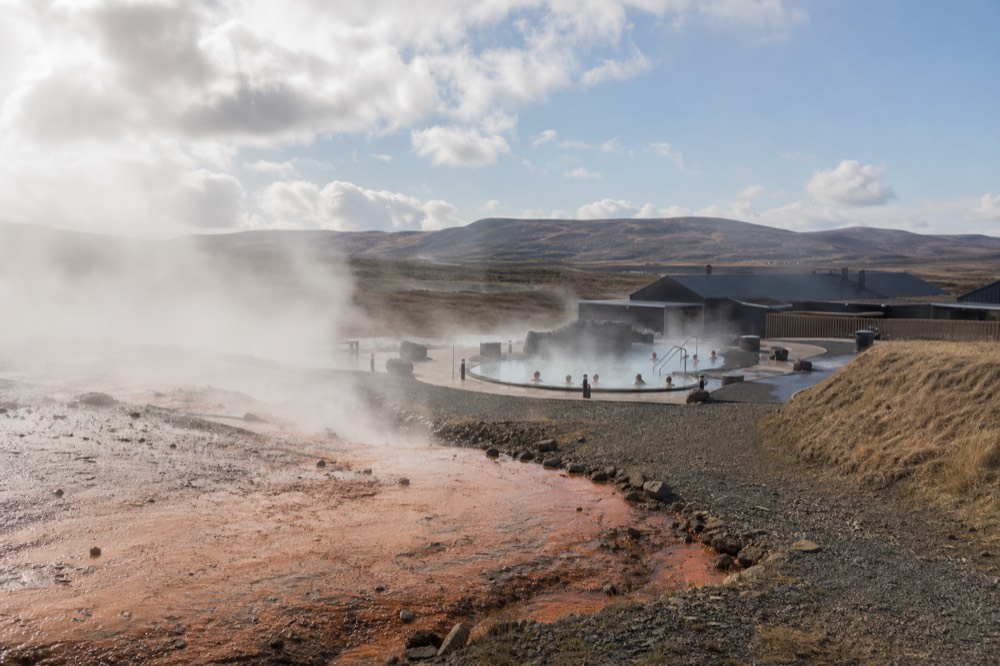 Steam rising from pools beside a shallow river channel under a wide highland sky