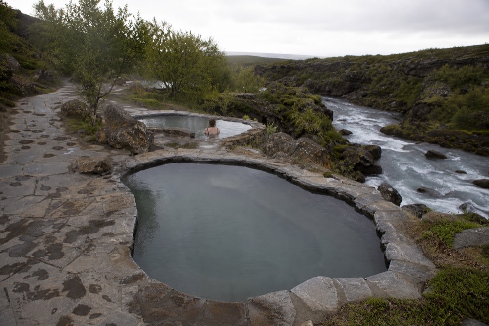 Two stone-lined geothermal pools on a canyon ledge above a rushing stream