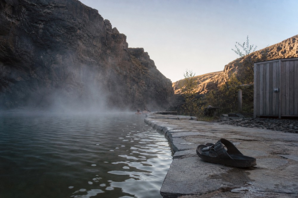 Flagstone-edged geothermal pool with steam drifting across dark canyon rock