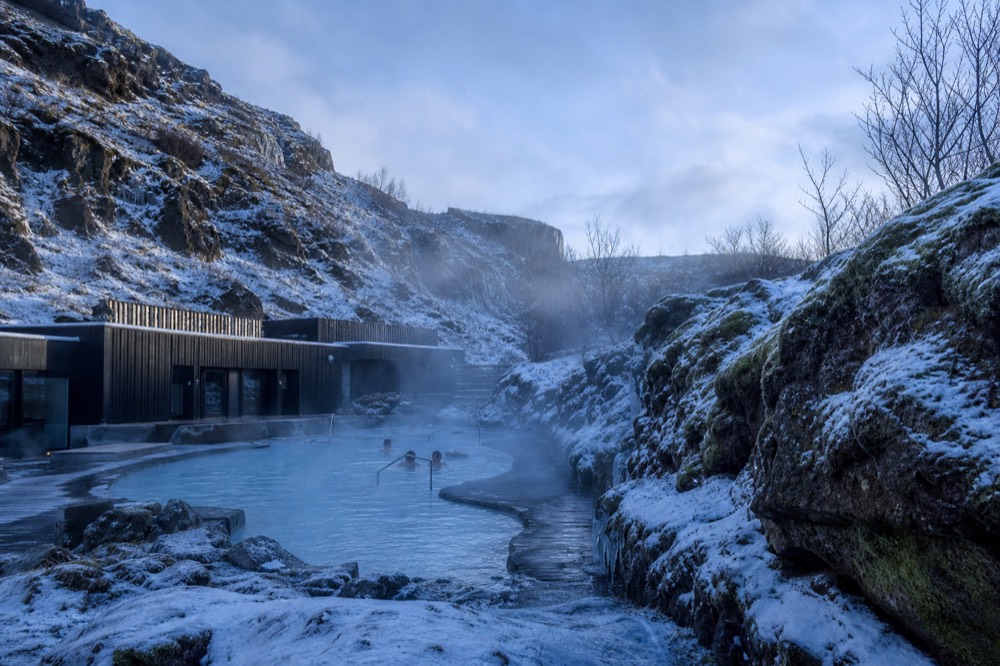 Snow-dusted canyon walls above a steaming geothermal pool in winter light