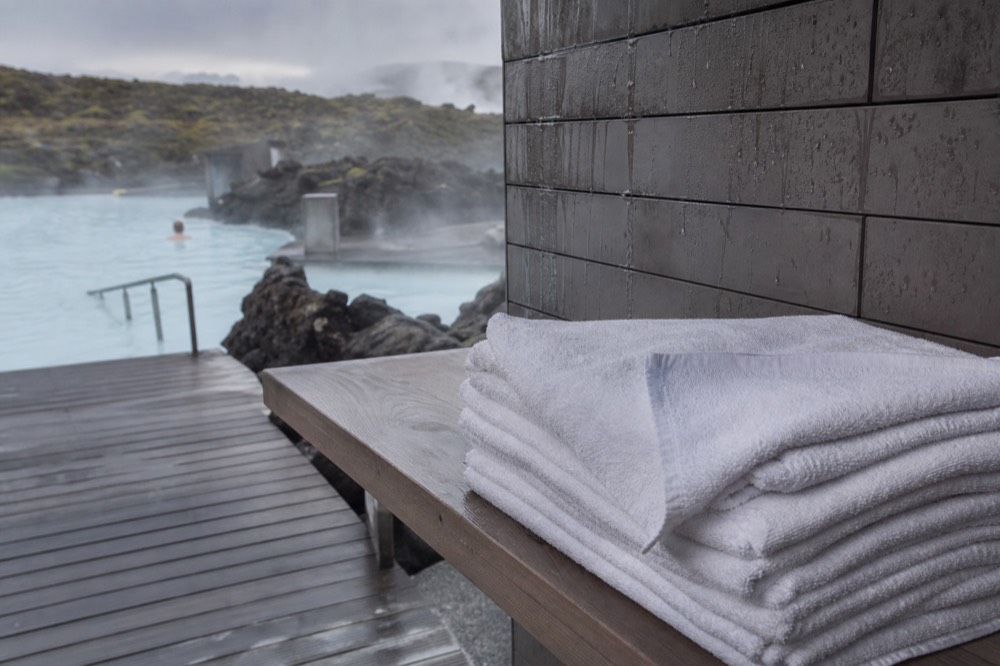 A stack of folded white towels on a wooden shelf beside a geothermal pool