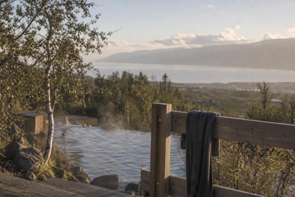 A towel draped over a wooden railing beside a steaming geothermal pool with mountains in the distance