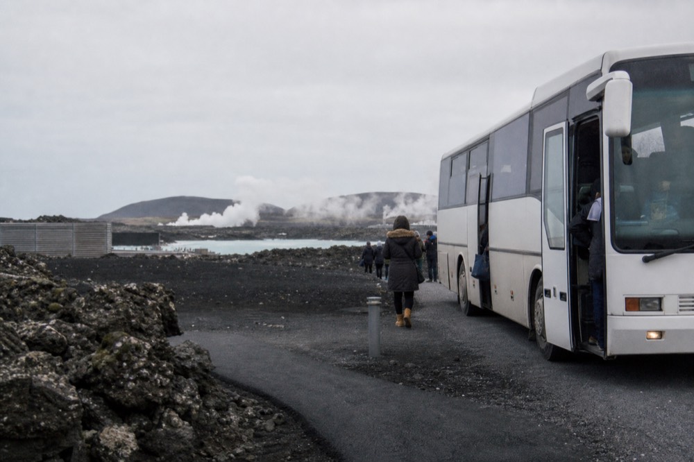 A coach bus parked outside a lagoon entrance with passengers disembarking