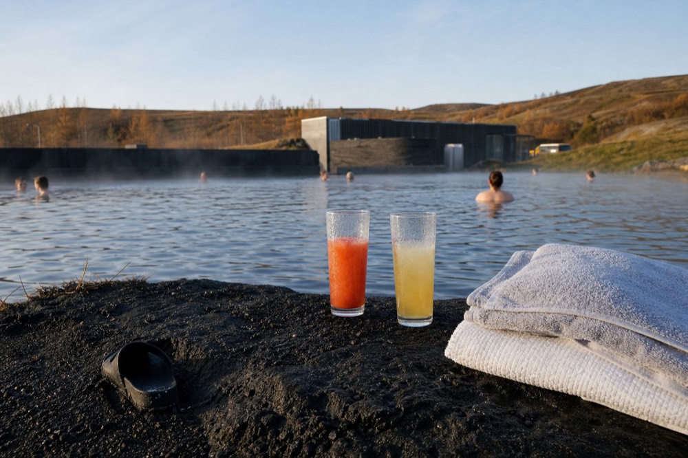 Two drinks resting on the edge of a steaming outdoor geothermal pool beside folded towels