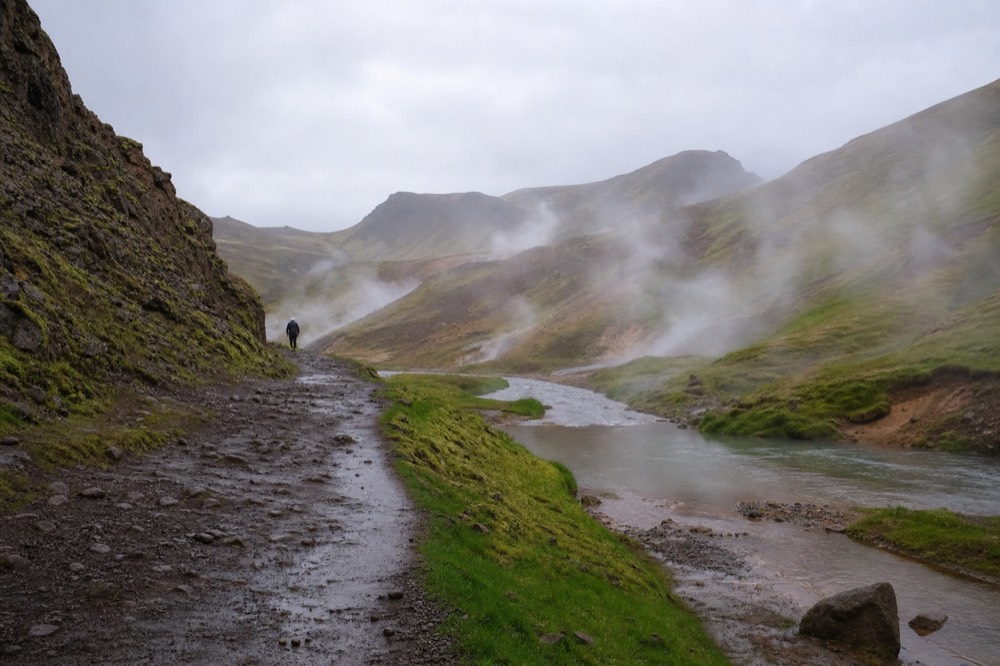 A shallow warm river winding through a green valley with steam drifting across the water