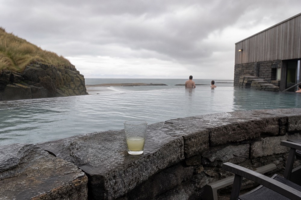 A geothermal infinity pool at the edge of a dark lava shoreline overlooking open sea