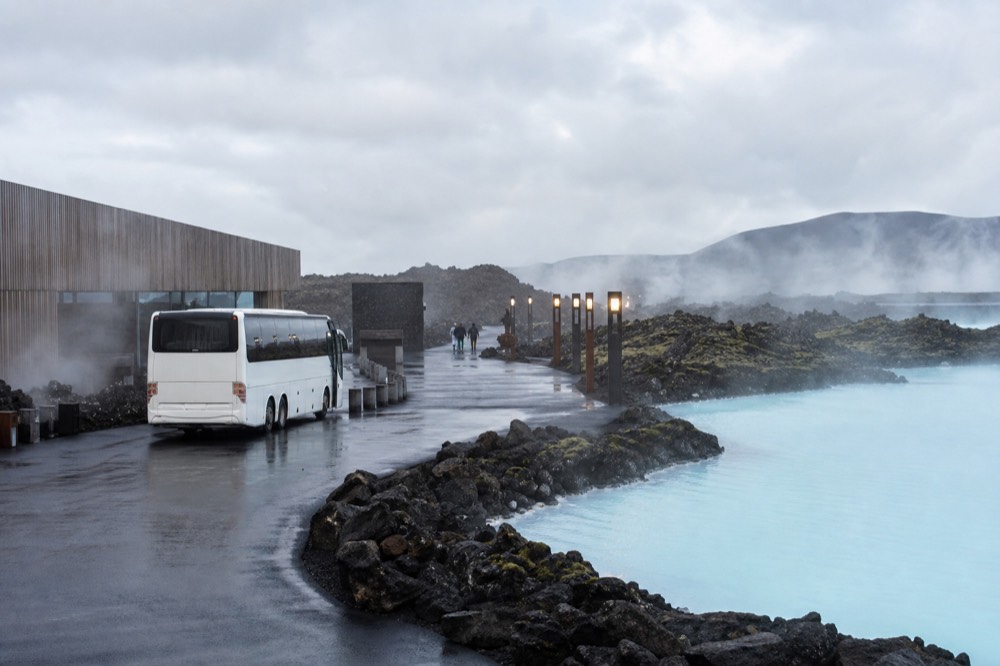 A coach parked beside a geothermal spa entrance building in rural Iceland