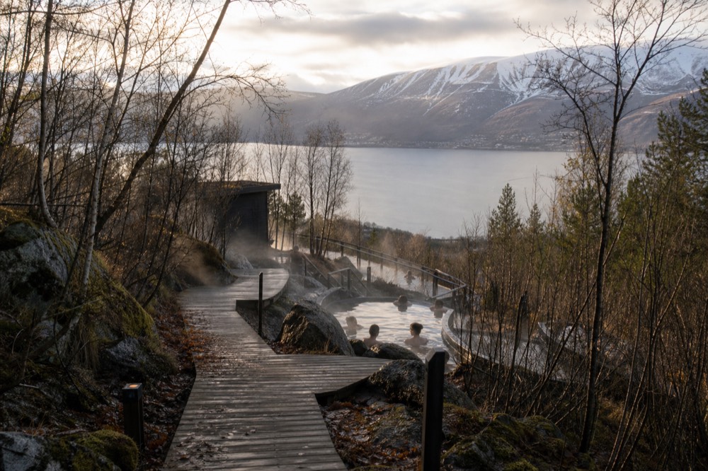 A wooden boardwalk leading between steaming pools at a geothermal bathing area