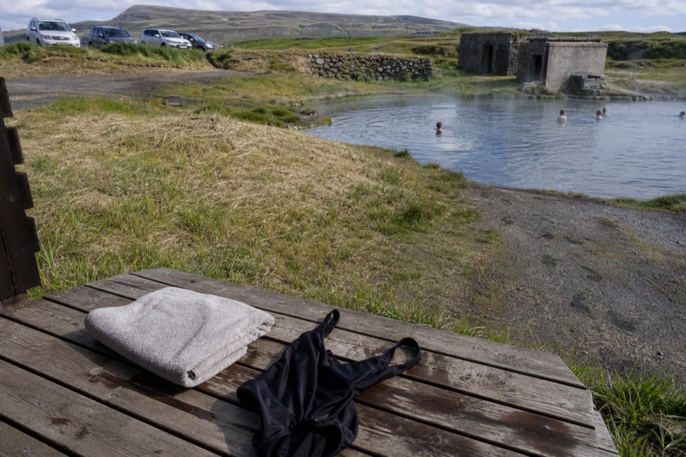 A folded towel and swimsuit on a wooden bench beside a geothermal pool