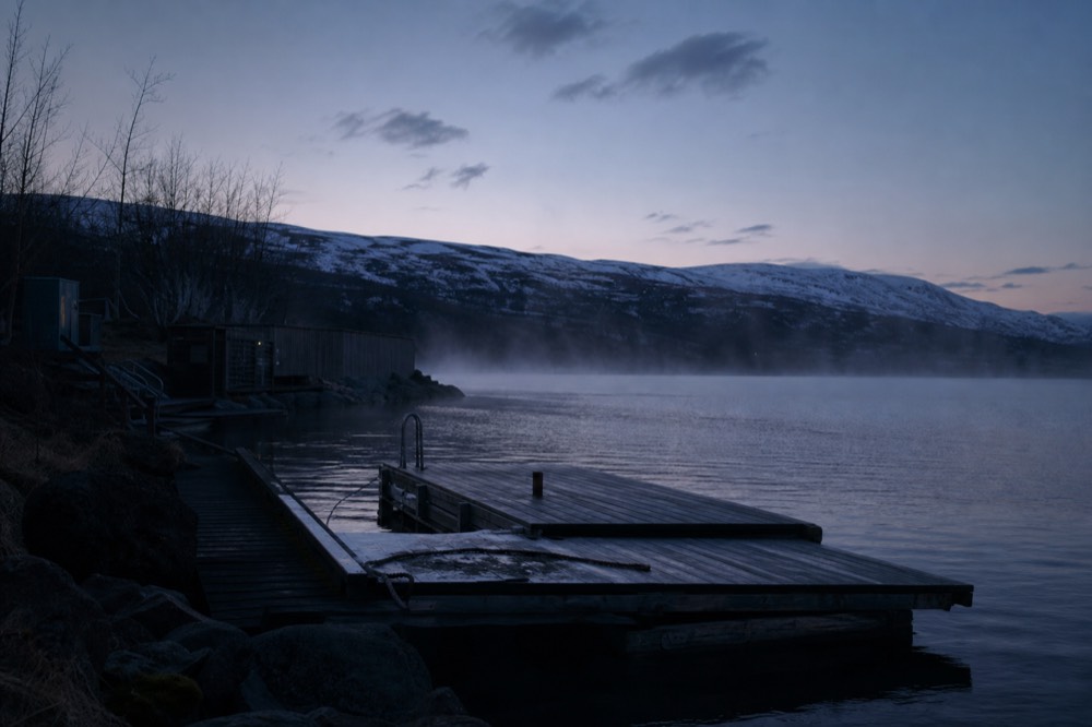 An empty geothermal pool at dusk with steam drifting across still water