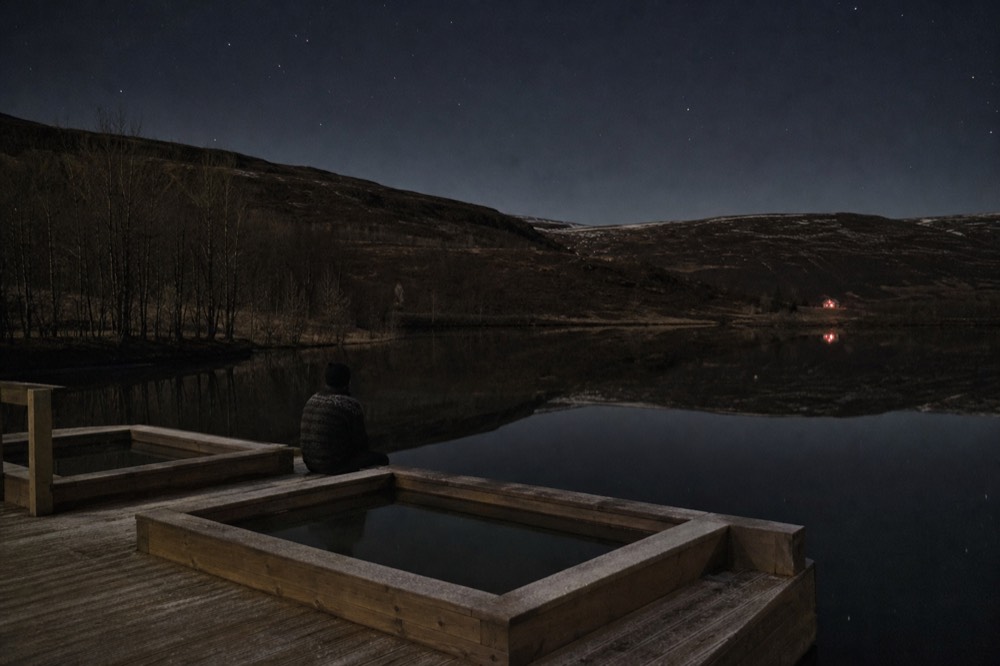 A fjord in West Iceland at night with still water and dark hills on both sides