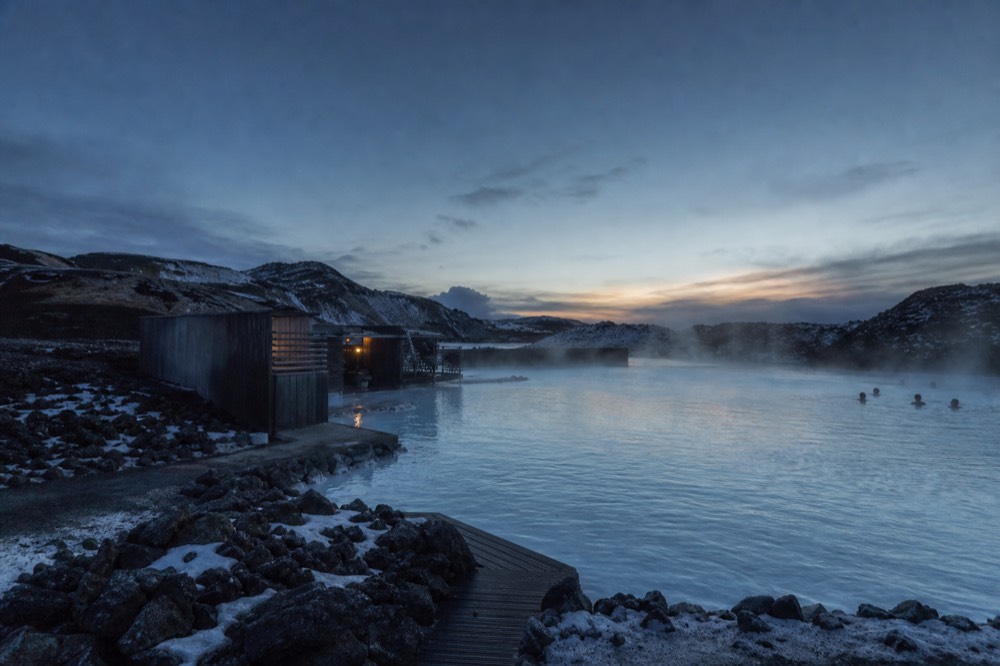 Steam rising from a geothermal lagoon beside a dark volcanic landscape in North Iceland
